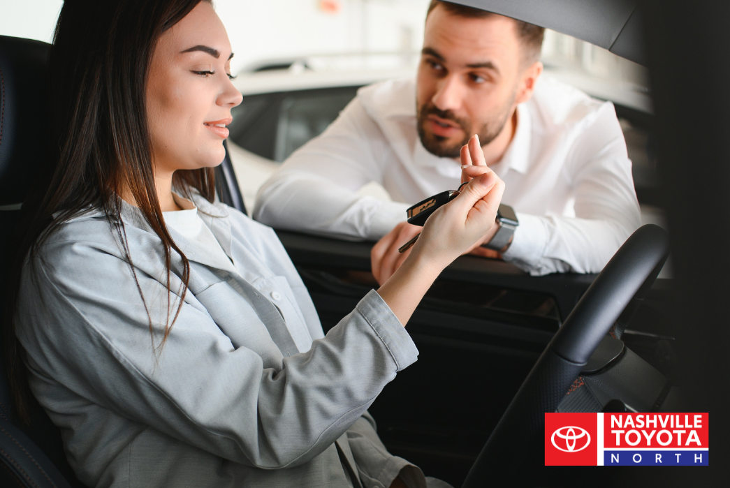 Two people one sitting in the driver's seat of a car and the other leaning in the window