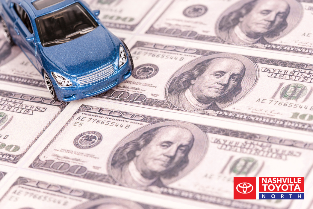 A toy blue car is on top of several one hundred dollar bills.