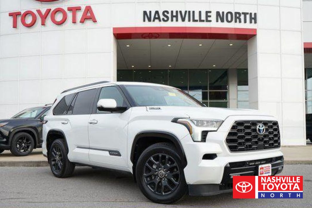 A white Toyota Sequoia SUV is parked in front of a Toyota dealership with the "Nashville North" sign visible. Another black SUV is parked to the left of the Toyota Sequoia.