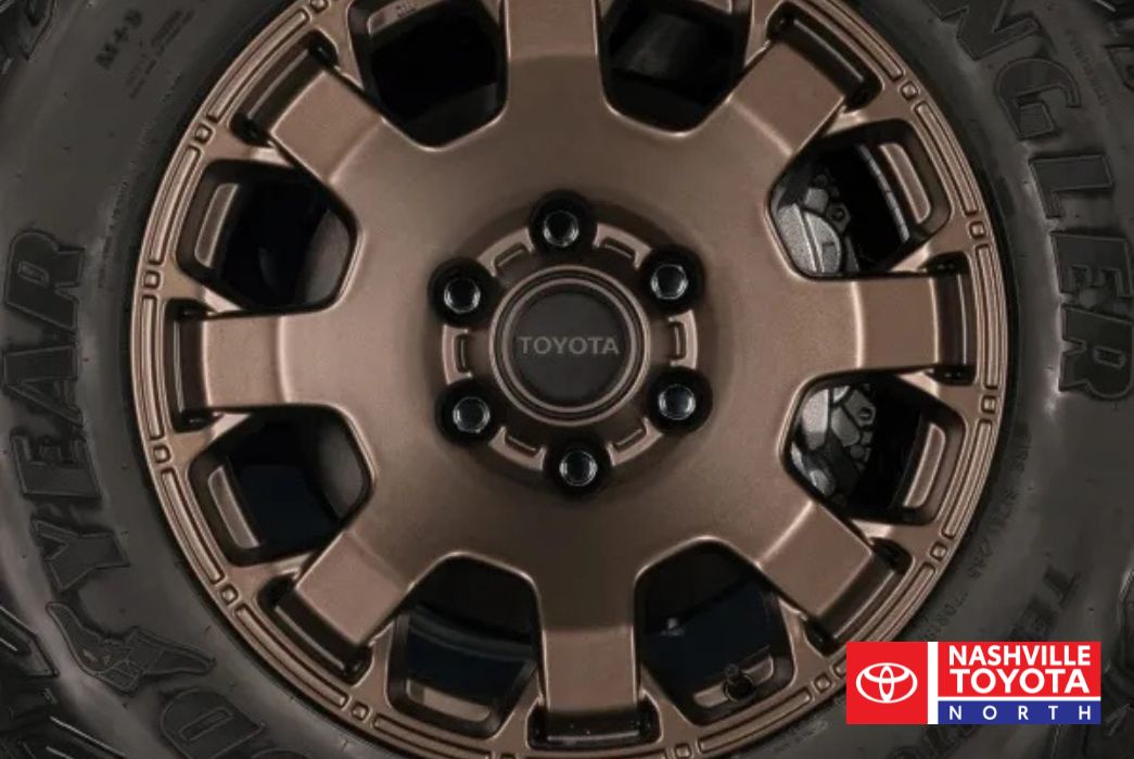 A close-up of a bronze Toyota wheel with black lug nuts and a Goodyear Wrangler tire.