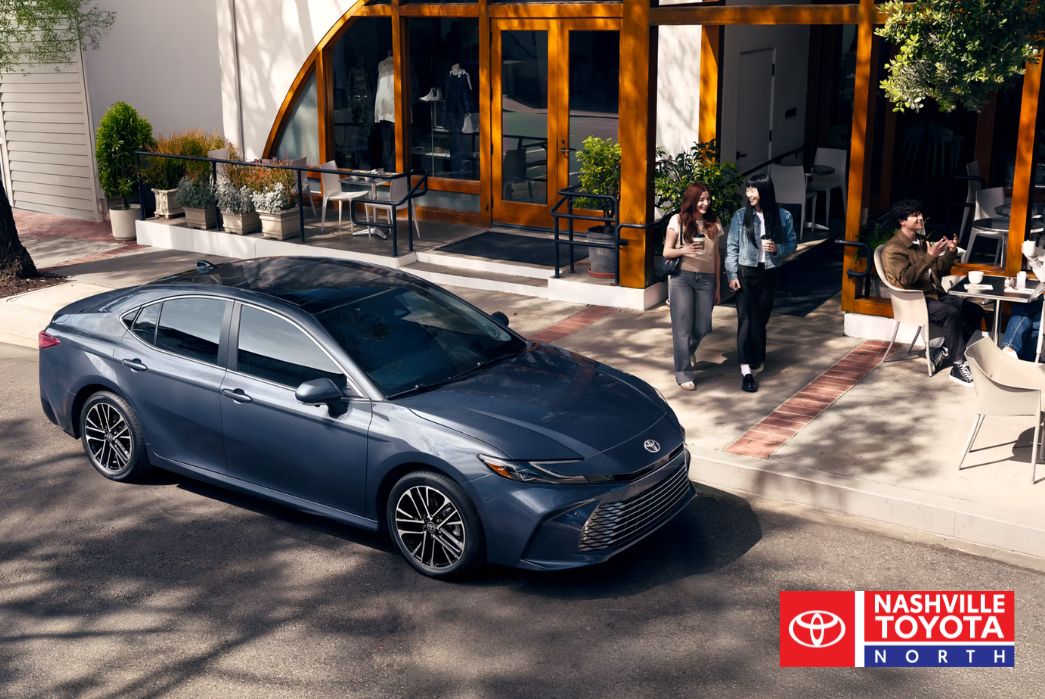 A dark blue sedan parked on the street in front of a cafe with people sitting outside.